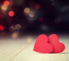 two red hearts sitting on top of a wooden table next to a blurry background