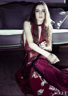 a woman in a red dress sitting on the floor next to a couch with pillows