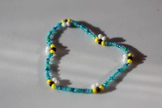 a blue beaded necklace with yellow and white beads is shown on a gray surface