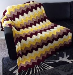 a couch with a blanket on top of it next to a black chair and wall