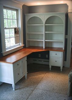 an empty room with a desk and bookcases in front of a window,