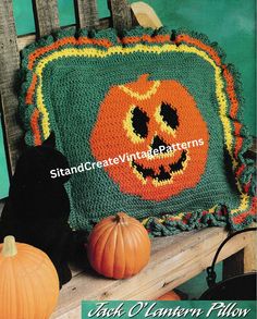 a crocheted pumpkin pillow sitting on top of a wooden bench next to a black cat