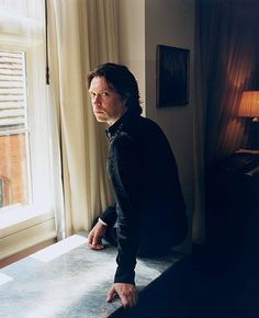 a man leaning on a window sill in front of a lamp and looking out the window