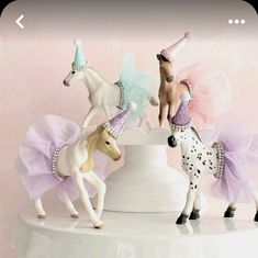 three toy horses are standing on top of a white cake plate with pink and blue tulle