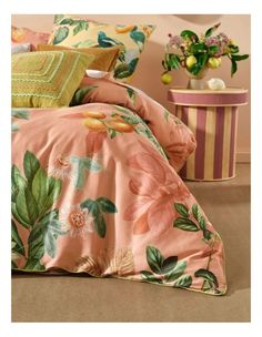 a bed covered in pink and green floral comforter sets next to a vase with flowers