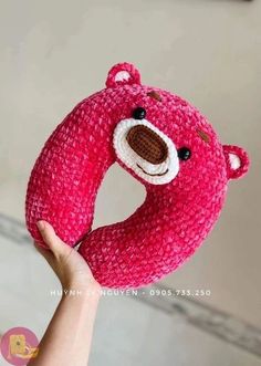 a hand holding a pink crocheted teddy bear in the shape of a donut