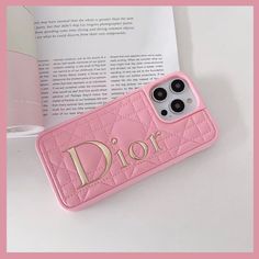 a pink phone case with the word dior on it next to an open book