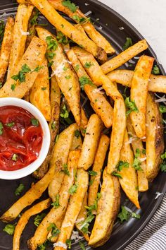 french fries with ketchup and parmesan on a black plate next to a bowl of ketchup