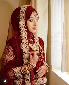 a woman in a red and gold bridal outfit standing next to a window with her hands on her hips