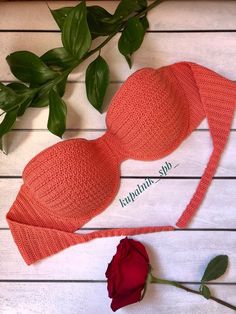 an orange bra and rose on a white wooden surface with green leaves next to it