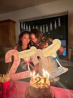 two women standing next to each other in front of a cake with candles on it