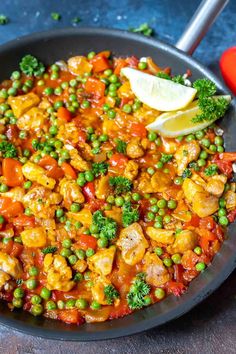 a skillet filled with chicken, peas and broccoli on top of a table