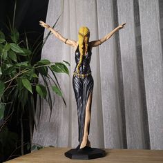 a statue of a woman standing on top of a wooden table next to a plant