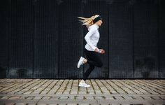 a woman is running on the sidewalk in white shirt and black leggings with her hair blowing back