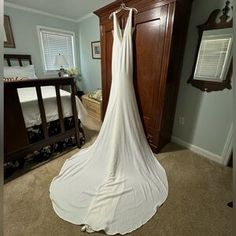 a white wedding dress hanging on a bed in a room with a dresser and mirror