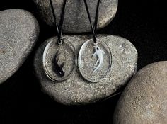 two pendants are sitting on some rocks and one is in the shape of a fish