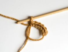 a piece of yarn with a wooden crochet hook attached to it on a white surface