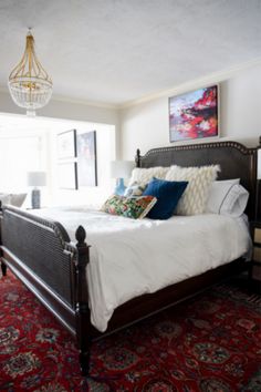 a bedroom with a bed, rug and chandelier hanging from the ceiling in front of a window