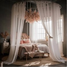 a bedroom with sheer curtains, a bed and a table in front of the window