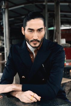 a man sitting at a table with his hand on his chin, wearing a suit and tie