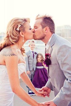 a bride and groom kissing each other in front of their wedding party on the beach