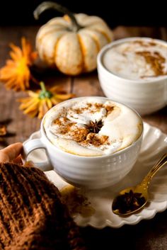 two white cups filled with hot chocolate and cinnamon on top of a saucer next to pumpkins