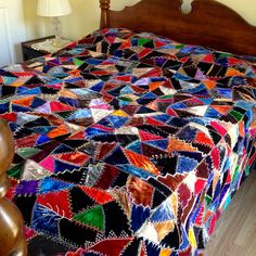 a bed with a multicolored quilt on it's headboard and foot board