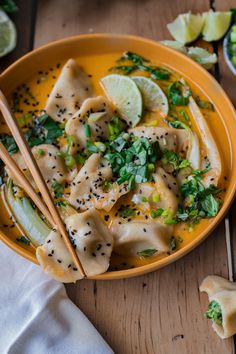 a yellow bowl filled with dumplings and topped with sliced limes next to two chopsticks