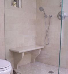 a white toilet sitting next to a walk in shower with a bench on the side