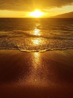 the sun is setting over the ocean with waves coming in to shore and sand on the beach