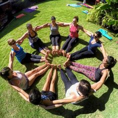 a group of people sitting in a circle on top of a grass covered field with their hands together