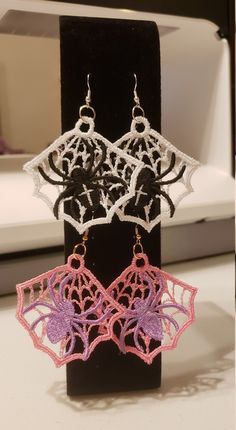 two pairs of earrings on display in front of a black stand with white and pink lace