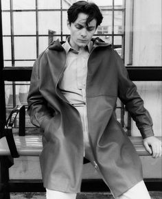 black and white photograph of a man sitting on a bench with his hands in his pockets