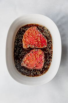 two pieces of meat are in a bowl with some seasoning on the side and black pepper sprinkles