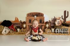 a baby sitting on the floor in front of a cake with cowboy decorations around it