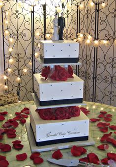 three tiered wedding cake with red roses on the table and lights in the background