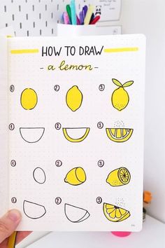 a hand holding up a notebook with lemons and lemonade drawings on the pages