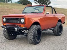 an orange pick up truck parked on top of a gravel road