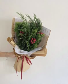 a bouquet of greenery wrapped in brown paper and tied with red ribbon, held by a woman's hand