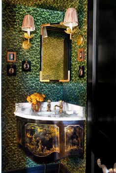 a fancy bathroom with green wallpaper and gold accents on the sink area, along with two lamps