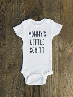 a white baby bodysuit with the words mommy's little schitt printed on it