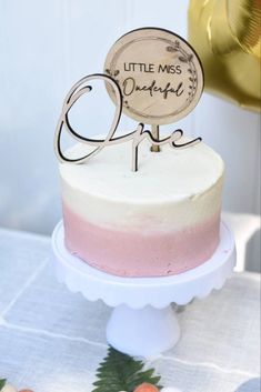 a little miss cake is decorated with pink and white frosting, wooden nameplate