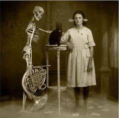 a woman standing next to a table with a cat sitting on top of it in front of a skeleton