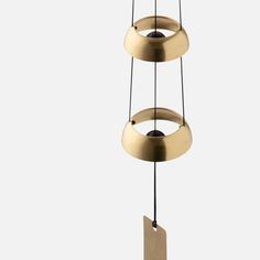 three circular light fixtures hanging from strings on a white background, one is gold and the other is black