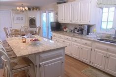 a large kitchen with white cabinets and marble counter tops, along with an island in the middle