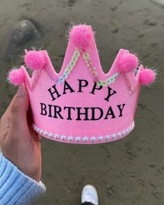 a hand holding a pink birthday crown with pom - poms