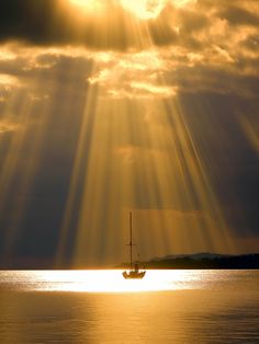 the sun is shining down on a sailboat in the water with clouds above it