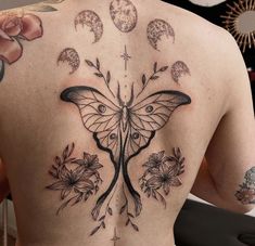 the back of a woman's tattoo with flowers and a butterfly on her left side