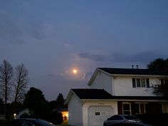 cars parked in front of a house with the moon rising over it's horizon