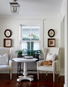 two white chairs and a table with a cat sitting on it in front of a window